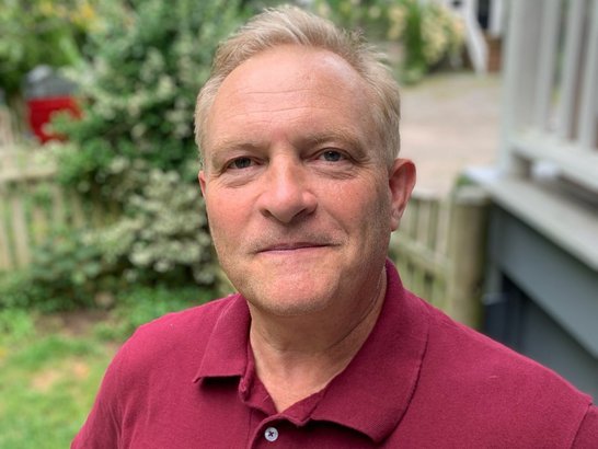 Christopher Woodin, wearing a red shirt and smiling.