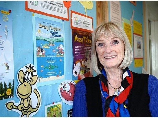 Pat Jones, smiling while stood in front of the notice board in Belgrave School.