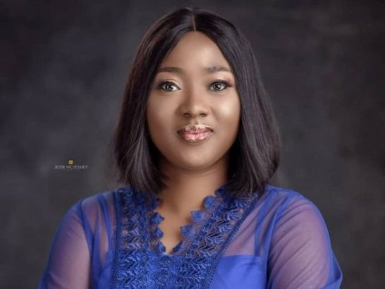 Lola Aneke, wearing a purple shirt and smiling for a professional photograph.